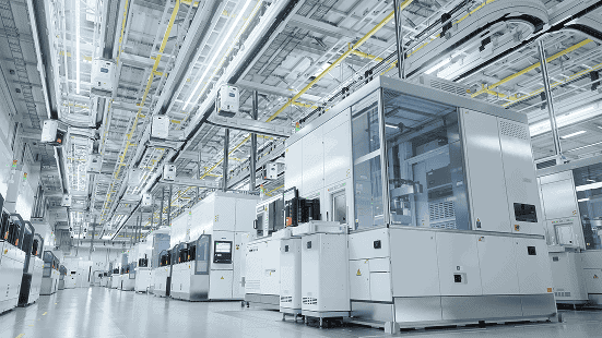 Large clean, high-tech industrial facility floor with rows of automated production machines and equipment under bright overhead lighting.